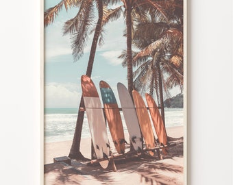 May include: Five surfboards leaning against a rack on a sandy beach with palm trees in the background. The surfboards are various shades of brown and orange with blue accents.