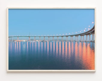 May include: A long, curved bridge with lights reflecting in the water at dusk. The bridge is made of concrete and has a green railing. There are boats moored in the water below the bridge.