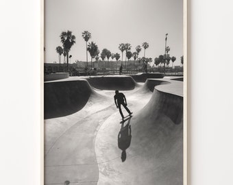 May include: Black and white photograph of a skateboarder performing a trick in a skate park. The skate park is made of concrete and has a variety of ramps and rails. The skateboarder is wearing a black shirt and pants and is riding a skateboard with black wheels. The photo was taken from a high angle, looking down at the skateboarder.