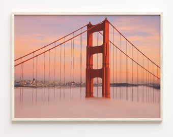 May include: A red suspension bridge with a tower rising above a layer of fog. The bridge is silhouetted against a pink and orange sunset sky.