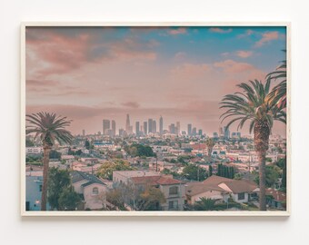May include: A panoramic view of the Los Angeles skyline with palm trees in the foreground. The city is bathed in a soft, pink and blue light, creating a dreamy atmosphere. The buildings are tall and modern, with a mix of residential and commercial structures. The palm trees are silhouetted against the sky, adding a touch of tropical beauty to the scene.