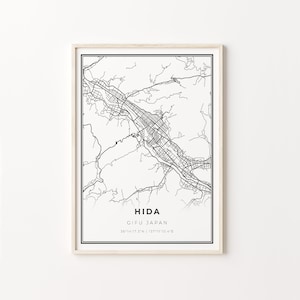 Puede incluir: Impresión enmarcada en blanco y negro de un mapa de Hida, Gifu Japón. El mapa presenta contornos detallados de calles y geografía. El texto "HIDA, GIFU JAPAN" está centrado en la parte inferior, con coordenadas. El marco es de color madera clara.
