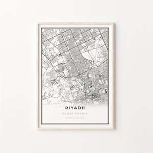Op de afbeelding: Zwart-witte kaartprint van Riyad, Saoedi-Arabië, met de naam van de stad en de coördinaten rechtsonder. De kaart is ingelijst in een licht houten lijst.