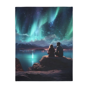 May include: A throw blanket featuring a scenic illustration of the aurora borealis over a lake. The design includes a couple sitting on a rock, silhouetted against the vibrant green and blue lights of the night sky.
