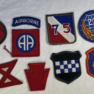 Puede incluir: Una colección de ocho parches bordados en varias formas y diseños. Los parches presentan una gama de colores, incluyendo rojo, azul, blanco y negro. Algunos parches tienen texto, como "AIRBORNE" y el número "75".