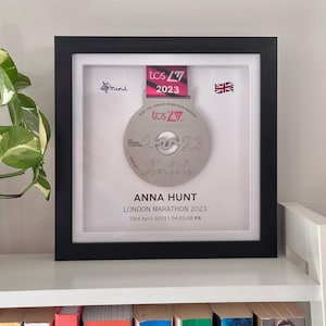 Könnte beinhalten: Eine gerahmte Silbermedaille mit einem rosa und weißen Band. Die Medaille trägt den Text "2023 TCS London Marathon Finisher" und "2023". Der Rahmen enthält auch eine kleine Union Jack Flagge und den Text "Anna Hunt, London Marathon 2023, 23rd April 2023 | 04:52:58 PB".