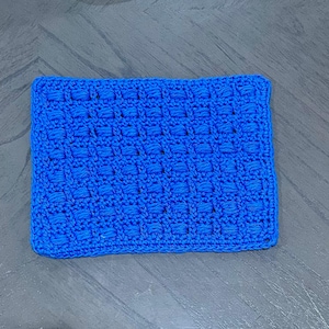 Puede incluir: Un artículo rectangular de ganchillo azul brillante con un patrón texturizado en relieve. Los bordes están cuidadosamente acabados con un borde sólido. La pieza hecha a mano es probablemente un paño de lavado o una pequeña manta.