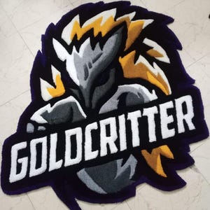 May include: A purple, black, white and yellow rug with a stylised creature and the text "GOLDCRITTER" in white.