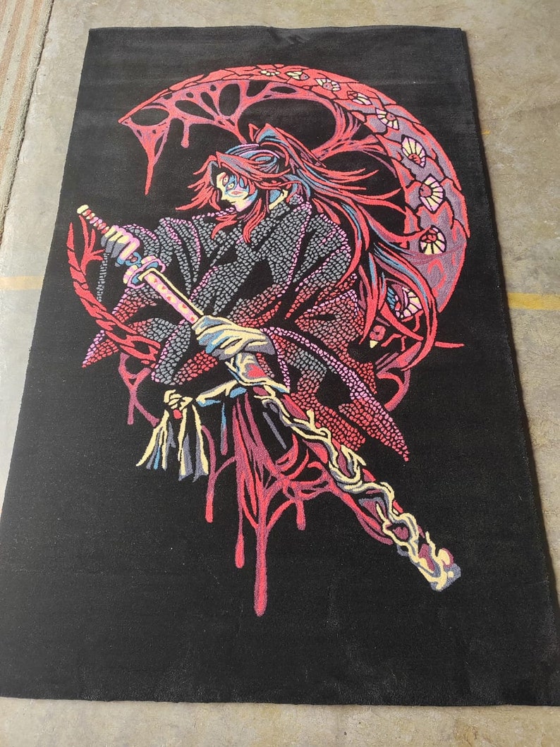 May include: A black rug featuring a red and pink design of a figure holding a sword. The figure has long red hair and is standing in front of a large, red, crescent moon.