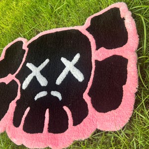 May include: A pink and black rug with a cartoon face with two X's for eyes and a frown.