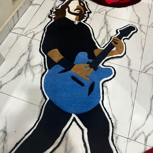 May include: A blue, black and white rug depicting a person playing a guitar. The rug is made of a soft, plush material.