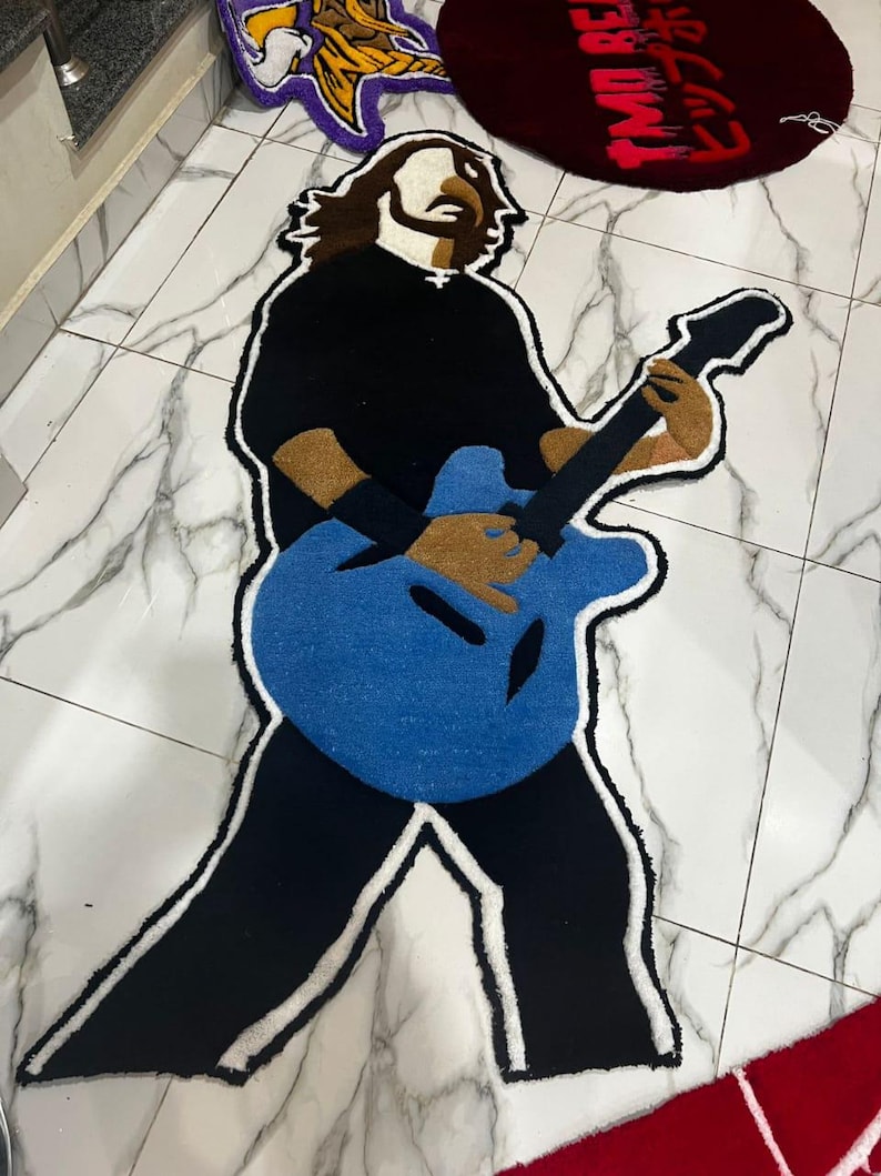 May include: A blue, black and white rug depicting a person playing a guitar. The rug is made of a soft, plush material.