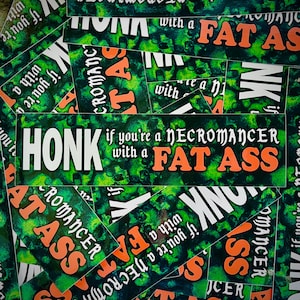 Peut inclure: Plusieurs autocollants rectangulaires avec un fond vert et noir. Le texte blanc et orange sur les autocollants dit : "HONK if you're a NECROMANCER with a FAT ASS". Les autocollants sont &eacute;parpill&eacute;s.