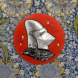 May include: A red circle with a black and white illustration of a knight's helmet with a visor. The helmet is surrounded by white stars.