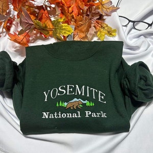 May include: A dark green sweatshirt with white embroidery that reads "Yosemite National Park". The embroidery also includes a brown bear and green trees.