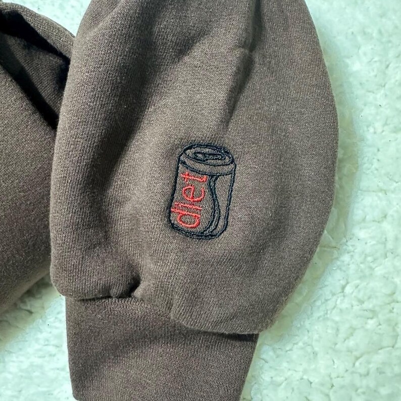 May include: Brown sweatshirt with a black and red embroidered image of a can of soda with the word "diet" on it.