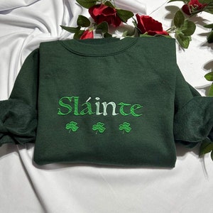 May include: A dark green sweatshirt with the Irish phrase "Sláinte" embroidered in white and green, with three shamrocks below the text.