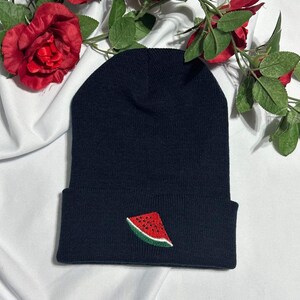 Puede incluir: Gorro negro con una sandía roja y verde bordada en la parte delantera.