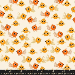 May include: A cream-colored fabric featuring a repeating pattern of small, orange goldfish with large black eyes and flowing fins. A black ruler with white markings and the text Ruby Star Society is visible along the bottom edge of the fabric.