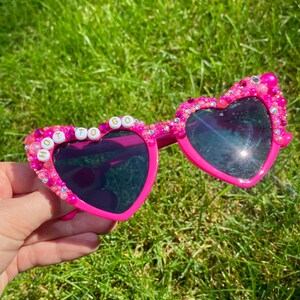 May include: Pink heart-shaped sunglasses with rhinestones and the words "HOT TO GO" spelled out in white letters.
