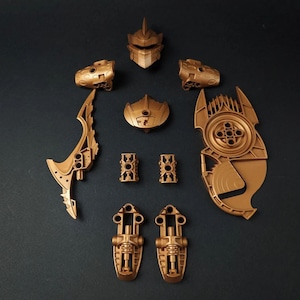 Op de afbeelding: Een set van goudkleurige plastic speelgoedstukken, waaronder een helm, armen, benen, een zwaard, een schild en andere stukken. De stukken zijn allemaal in gedemonteerde staat.