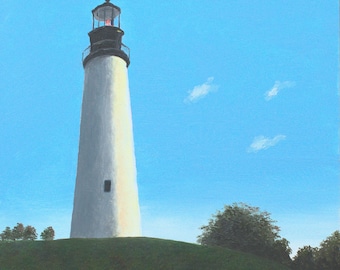 May include: A white lighthouse with a black roof and a black lantern room stands tall against a bright blue sky with a few small white clouds. The lighthouse is on a grassy hill with green trees in the foreground.