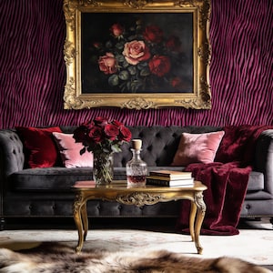 Può includere: Un lussuoso salotto con un divano grigio scuro trapuntato, cuscini di velluto e una coperta rossa. Un dipinto di rose con cornice dorata è appeso sopra. Un tavolino dorato espone rose e una caraffa di vetro.