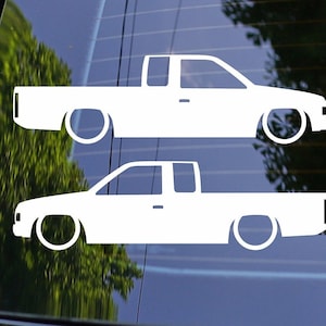 May include: Two white silhouette decals of a pickup truck on a blue background. The trucks are facing the right side of the image. The decals are for a car window.