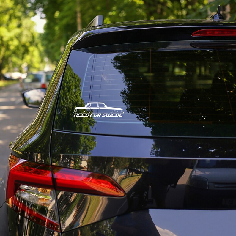 May include: A black car with a white sticker on the back window. The sticker features a white silhouette of a car and the text "Need for Swede".
