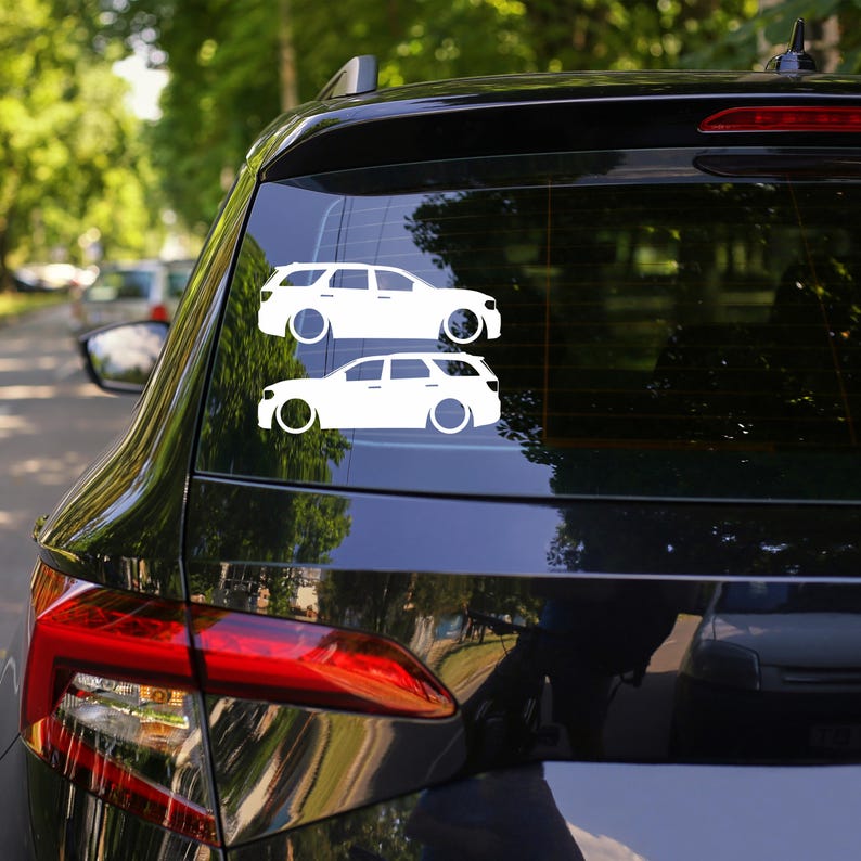May include: Two white car decals are displayed on the rear window of a black vehicle. The decals depict a side profile of a station wagon with large circular wheels. The car decals are a simple, minimalist design.