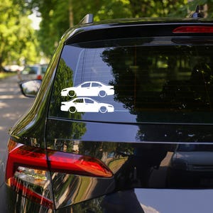 Könnte beinhalten: Ein schwarzes Auto mit einer weißen Silhouette von zwei Autos auf der Heckscheibe. Die Silhouette ist von einer Limousine und einem Kombi.
