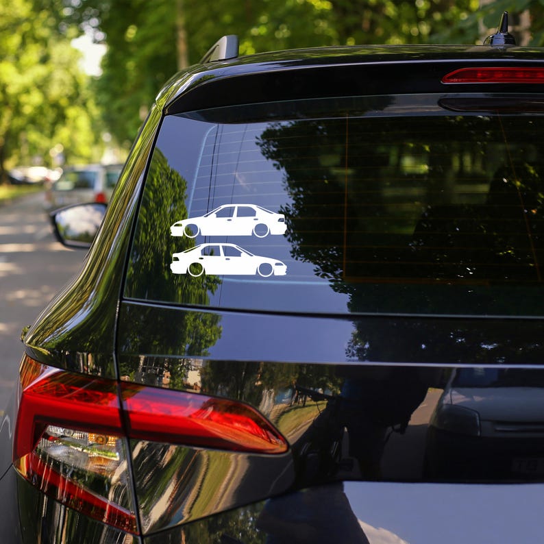 K&ouml;nnte beinhalten: Zwei wei&szlig;e Autoaufkleber sind auf der Heckscheibe eines schwarzen Fahrzeugs angebracht. Die Aufkleber zeigen das Seitenprofil einer Limousine in minimalistischem Design. Die Autoaufkleber sind ein schlichtes, sauberes Design, ideal f&uuml;r Autoenthusiasten.