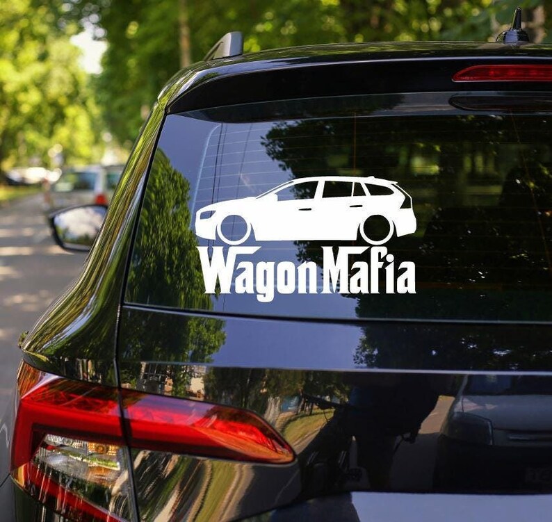 K&ouml;nnte beinhalten: Ein wei&szlig;er Vinyl-Aufkleber mit einer Silhouette eines Kombi-Autos und dem Text "Wagon Mafia". Der Aufkleber befindet sich auf der Heckscheibe eines schwarzen Autos.