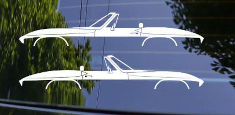 May include: Two white convertible car decals are displayed against a dark background. The decals are a minimalist design, featuring the car's outline with details like the windshield, wheels, and a small seat. The image is a close-up, highlighting the car's sleek shape.
