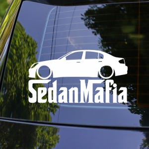 May include: White decal of a sedan car with the text "SedanMafia" in a bold font. The car graphic is a side profile, showing the wheels and body of the vehicle. The decal is designed for application on a car window.