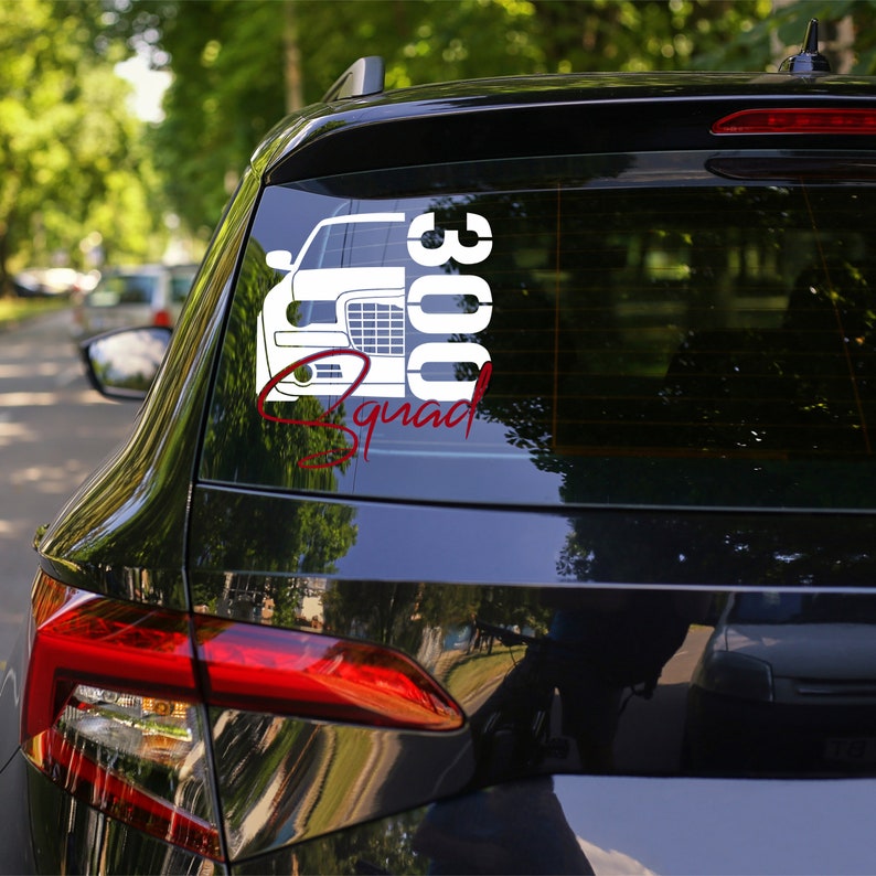 May include: A black car with a white vinyl sticker on the back window. The sticker features a white silhouette of a car with the number 300 and the word "Squad" written in red.