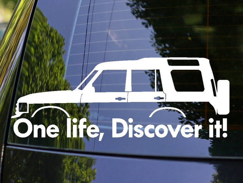 Peut inclure: Autocollant en vinyle blanc repr&eacute;sentant un Land Rover Discovery SUV avec le texte "One life, Discover it!" sur une vitre de voiture noire.