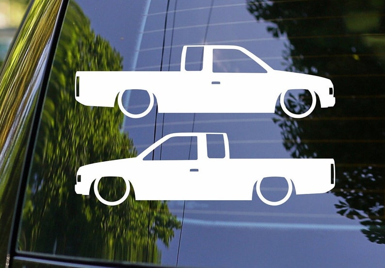 May include: Two white silhouette decals of a pickup truck on a blue background. The trucks are facing the right side of the image. The decals are for a car window.