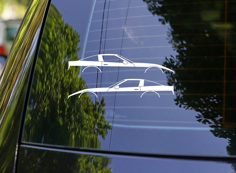 K&ouml;nnte beinhalten: Zwei wei&szlig;e Silhouette-Aufkleber eines Corvette-Autos auf einem blauen Autofenster.