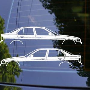 Pode incluir: Duas decalcomanias brancas para carro, cada uma representando um perfil lateral de um sedan. As decalcomanias s&atilde;o aplicadas em uma superf&iacute;cie escura e reflexiva, com uma &aacute;rvore verde desfocada ao fundo. O design do carro inclui detalhes das rodas e janelas.