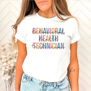 Könnte beinhalten: Weißes T-Shirt mit dem Text "BEHAVIORAL HEALTH TECHNICIAN" in bunten, übereinander angeordneten Buchstaben.