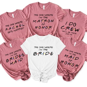 May include: Five t-shirts with the text "The One Where" and different roles for a wedding party. The shirts are in pink and white with colorful dots.