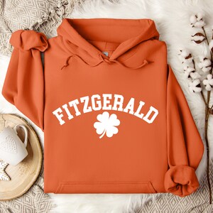 May include: Orange hoodie with a white four-leaf clover and the text "FITZGERALD" in a white arch.