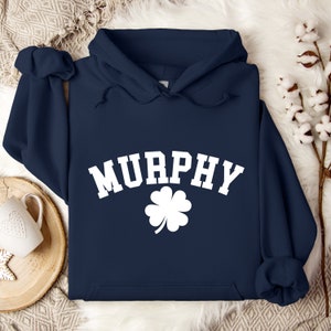 May include: Navy blue hooded sweatshirt with white text that reads "MURPHY" in an arched font with a white four-leaf clover underneath.