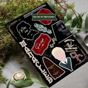May include: A black and gold sticker sheet featuring various Harry Potter themed designs, including a silhouette of a woman, a snake, a red rose, a wand, a key, a red and gold crest, and a portrait of a young man with blonde hair. The text "You are not replaceable" is visible on the sticker sheet.