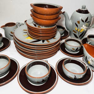 May include: A complete vintage ceramic dinnerware set. The set includes plates, bowls, cups, saucers, a teapot, and a creamer. The pieces are gray with brown rims and accents, and feature a floral design with yellow and white accents.