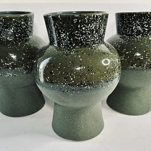 May include: Three green ceramic vases with a speckled white glaze. The vases are round and have a wide base.
