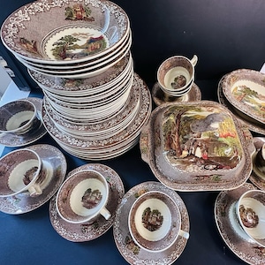 May include: A collection of brown and white vintage china with a landscape design. The set includes bowls, plates, saucers, cups, and a serving dish. The china has a floral border and a detailed scene in the center.