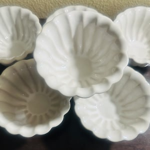 May include: Five white ceramic bowls with a fluted design. The bowls are arranged in a circle, with the largest bowl in the center.
