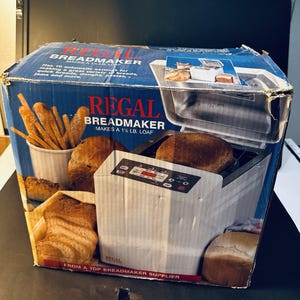 May include: A Regal breadmaker in its original box. The box is blue with images of bread and breadsticks. The breadmaker is white with a digital display. The box states it makes a 1 1/2 lb loaf.